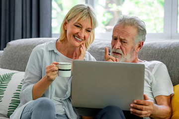 Senior couple using laptop in living room. White man and woman sitting on couch looking at laptop. Exciting mood.