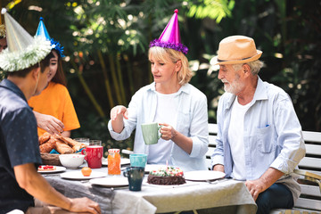 Senior birthday in. backyard tropical garden. White, asian senior man and woman with young couple. Enjoying a birthday party at home garden.