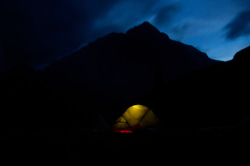 Night time view on campsite: a tent illuminated from the inside, sihoutte of mountains in the background