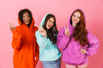 Pleased smiling young three multiethnic girls friends posing isolated over pink wall background...
