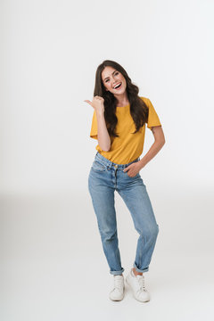 Full length image of young brunette woman wearing casual clothes smiling and pointing finger at copyspace