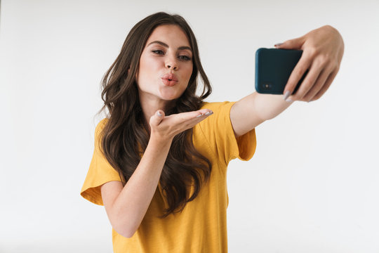Image of gorgeous brunette woman blowing air kiss at camera while taking selfie photo on cellphone