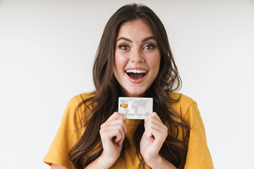 Image of astonished brunette woman wearing casual clothes smiling and holding credit card