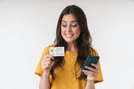 Image of pleased brunette woman wearing casual clothes holding credit card and cellphone