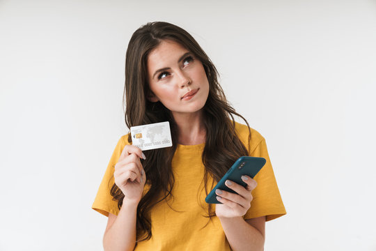 Image of thoughtful brunette woman wearing casual clothes holding credit card and cellphone