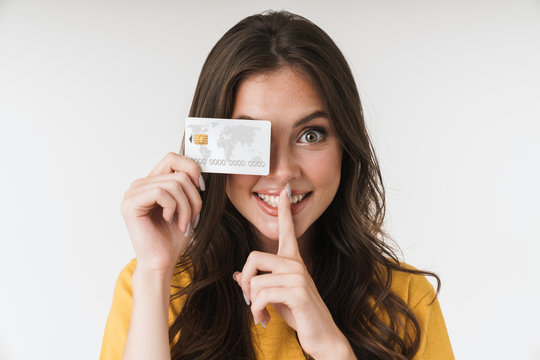 Image of happy brunette woman wearing casual clothes keeping finger at lips and holding credit card