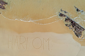 Aerial top shot from ocean waves and handwritten Hari Om at the beach