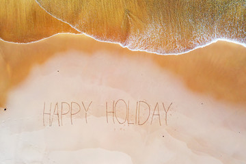 Aerial top shot from ocean waves and handwritten Happy holiday at the beach