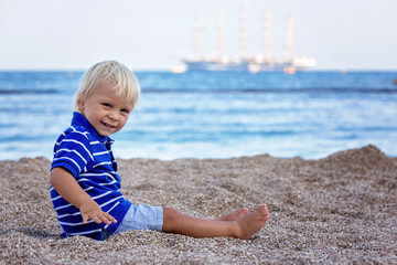 Fototapeta na wymiar Toddler child, sitting on beach, watching lighted ship in the ocean