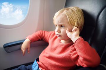 Capricious kid traveling by an airplane. Dissatisfied little boy sitting by aircraft window during...