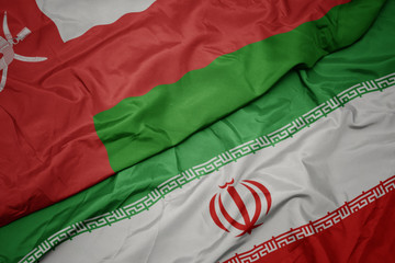 waving colorful flag of iran and national flag of oman.