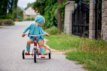 Adorable toddler boy with knitted outfit, riding tricycle on a quiet village street