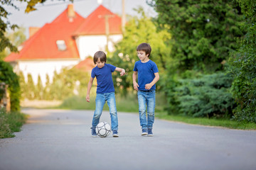 Two cute little kids, playing football together, summertime. Children playing soccer