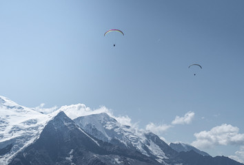 Two Parachouttes going side to side in the blue sky with clouds in the French Alps, Chamonix during a summer tour, fly and sport.