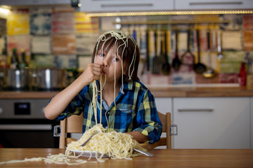 Little preschool boy, cute child, eating spaghetti for lunch and making a mess