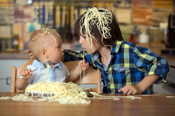 Little baby boy and his older brother, toddler child, eating spaghetti for lunch and making a mess