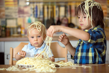 Little baby boy and his older brother, toddler child, eating spaghetti for lunch and making a mess