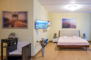 Modern interior of light studio apartment. View of the bed. TV and chair.
