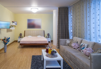 Modern interior of light studio apartment. Served table. King-size bed. Cozy sofa.