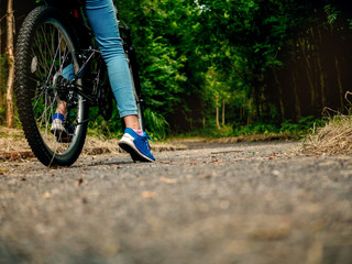 Teenager girl standing with her foot and bike on a path into dark scary forest. Concept risk evaluation, scary unknown, adventure, outdoors. Copy space.