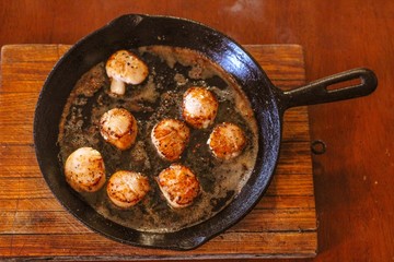Selective Focus closeup of perfectly seared fresh sea scallops in butter and cracked pepper, sizzling on a cast iron skillet