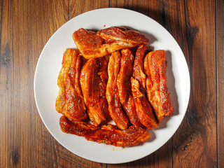 Pork belly ribs on a white plate marinated with Korean style souse, Top view.