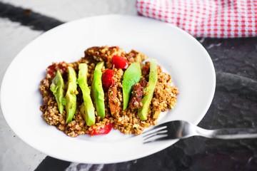 Buckwheat, avocado and red pepper on plate on table.