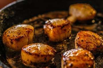 Selective Focus closeup of perfectly seared fresh sea scallops in butter and cracked pepper, sizzling on a cast iron skillet