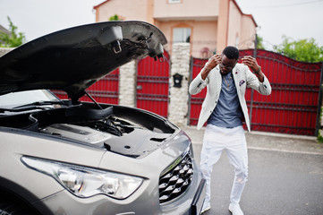 Stylish and rich african american man stand in front of a broken suv car needs assistance looking under opened hood.