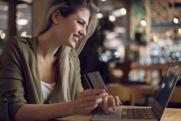 Young happy woman using credit card for online shopping in a cafe