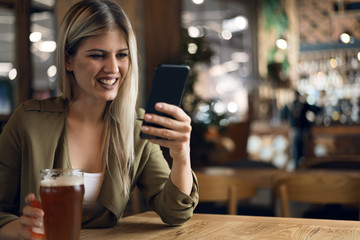 Happy woman reading text message on mobile phone while sitting in a bar