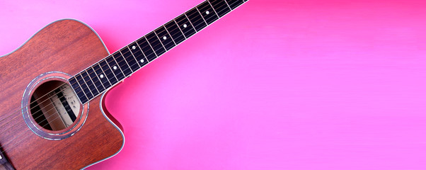 Acoustic guitar resting against a blank pink background with copy space.