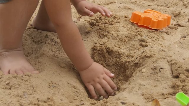 Toddler boy is playing with sand and moulds in sandbox. Baby walks with bare feet on children playground. Outdoor leisure activity,.