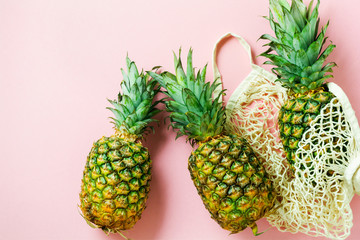 Fresh pineapples in mesh shopping bag on pink background. Zero waste concept. Top view.