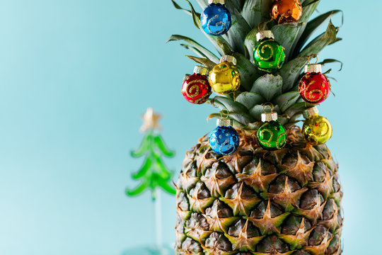 Christmas tree made of pineapple and colorful baubles on blue background, copy space. Card, decoration for new year party.