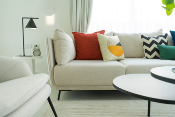 Large white sofa with colorful cushions in a spacious living room interior with green plants and white walls.