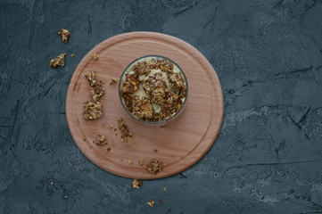 Obraz na płótnie Canvas Granola, banana, kiwi and greek yogurt. Dessert in glass cup on a wooden round board, dark background. Concept body and healthy food