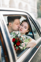 Bride with groom sitting in old black retro car. Newlyweds kissing and embracing while sitting inside old black retro car in old city center. Lviv, Ukraine