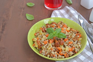 Pearl barley with chanterelles and vegetables in a green bowl on a dark brown concrete background. Recipes with seasonal chanterelle mushrooms. Cooking wild mushrooms.