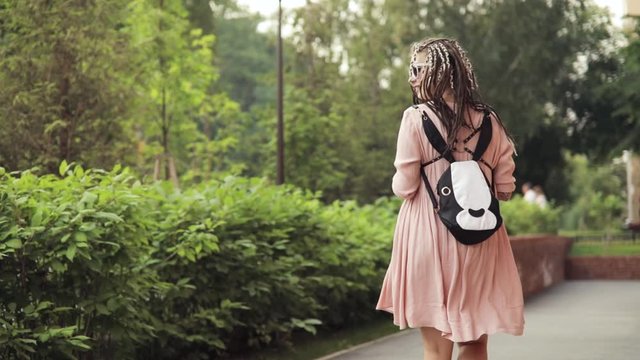 Maternity leave. Pregnant happy young woman hipster walking in city park with coffee in hands. She turning looking at camera and smiling. She enjoying her pregnancy. She is in cute dress with braids.