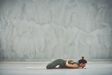 Middle aged Caucasian brunette in green outfit lying on stomach with hands behind backs. Yoga practicing concept.