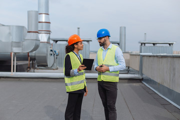 Construction industry charismatic African woman engineer using a tablet to analyzing the plan of construction site with the foreman, good looking man holding a ration, have a discussion with engineer