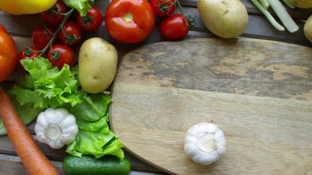 Top view of male hand spinning head of garlic on wooden cutting board on kitchen table with fresh vegetables