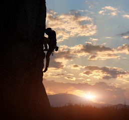 Side view of strong rock climber at dawn. Male silhouette on high rocky wall having extreme...