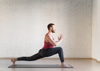 Warrior pose. Caucasian fit man stands in deep stretching and doing yoga in fitness studio, side view, selective focus.