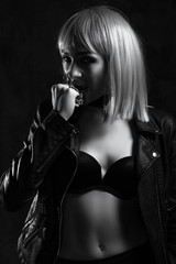 Fototapeta premium Girl in a leather jacket with white hair in an interior loft studio with a chain in her hands. The girl in the bra. Fashionable Female stands at the brick. Fashionable female with gray hair