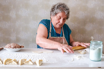 The old woman rolls the dough. Grandmother is cooking in the kitchen.
