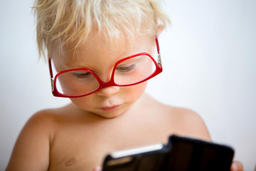 Sweet toddler boy with red eyeglasses on white background, making faces