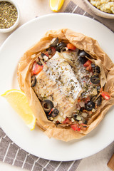 Fillet of white fish (Pollock, cod, sea bass, Dorada) with olives, tomatoes and lemon, baked in parchment. Traditional French food fish papillot and bulgur