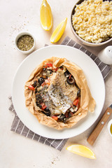 Fillet of white fish (Pollock, cod, sea bass, Dorada) with olives, tomatoes and lemon, baked in parchment. Traditional French food fish papillot and bulgur